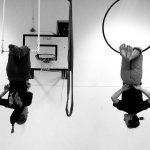 two aerialists hanging upside down in a hoop and trapez